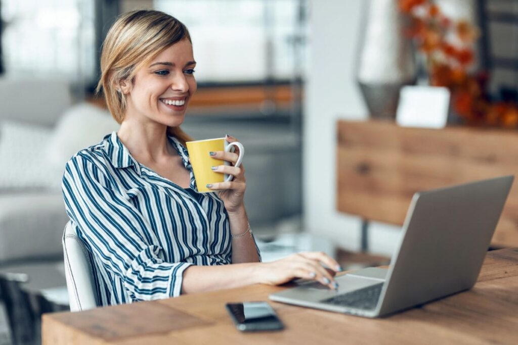 A freelancer drinking coffee while working from her home office on a laptop.