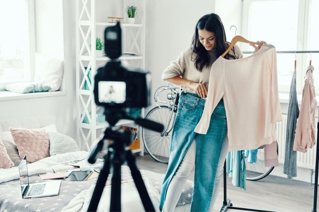 A woman video blogger is holding clothing items and recording a video for her YouTube channel.