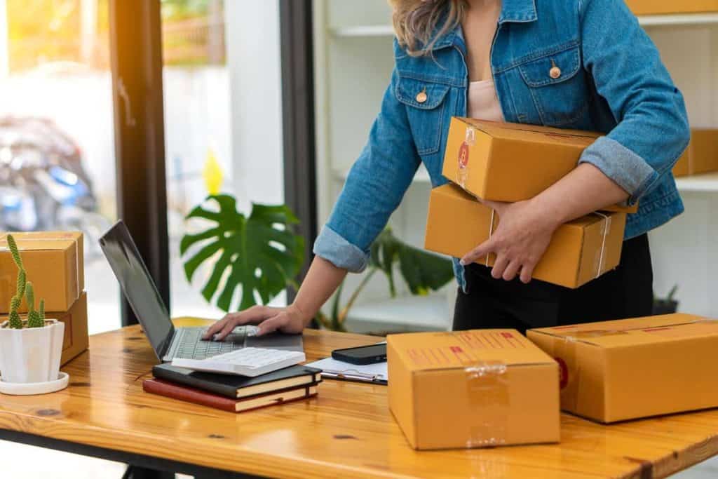 Online retail store owner checking orders on her laptop and sorting packages.