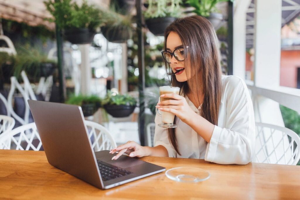 A woman working remotely from a cafe, using a laptop and drinking coffee.