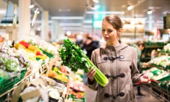 An Instacart Shopper picking up and looking at celery in a grocery store for blog post Instacart Shopper Review: What Working for Instacart Is Like