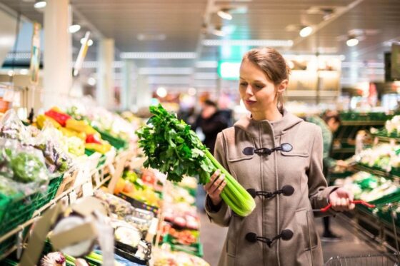 An Instacart Shopper picking up and looking at celery in a grocery store for blog post Instacart Shopper Review: What Working for Instacart Is Like