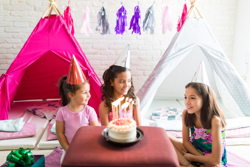 Little girls at a sleepover party with colorful decorations and a cake