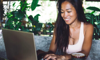 Long haired Asian woma working on her laptop drinking a latte looking for trusted money-making websites