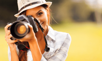 Young woman outside wearing a hat and taking photos with a camera
