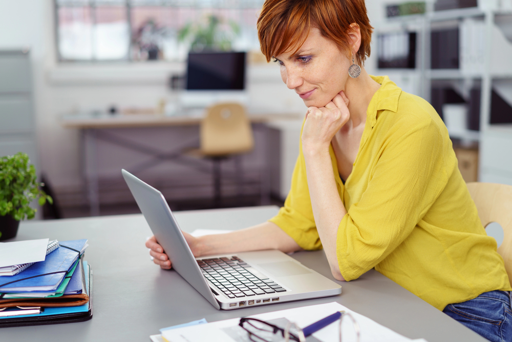 Middle aged woman with short hair reading an article on her latop titled 99 work at home career ideas for women