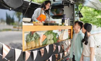 A woman working at a food truck, taking orders through the window.