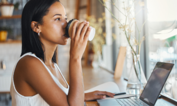 Pretty young freelance AI trainer drinking coffee and working on her laptop