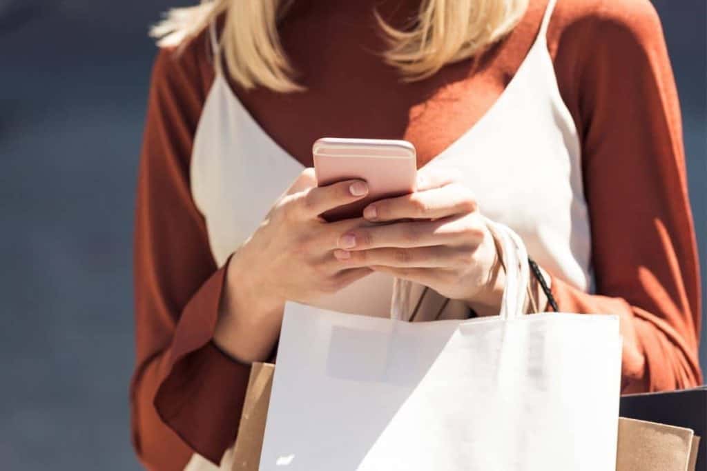 A woman holding shopping bags and looking at her phone while she shops.