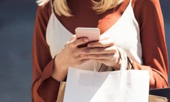 A woman holding shopping bags and looking at her phone while she shops.