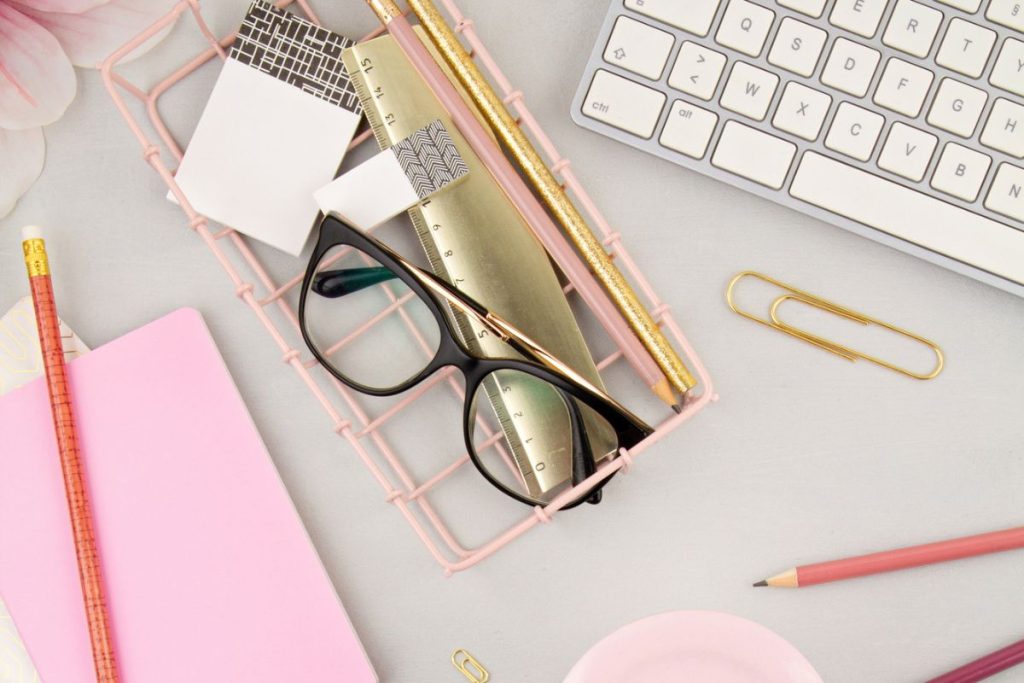 Still life of a home office desk, with a keyboard, glasses, and notebooks.