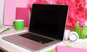 Feminine and colorful desk at home with laptop, pens, notebooks, and flowers