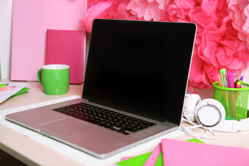 Feminine and colorful desk at home with laptop, pens, notebooks, and flowers