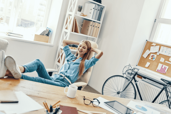 Young woman sitting in her office chair with her feet kicked up on her desk, with her bike in the background