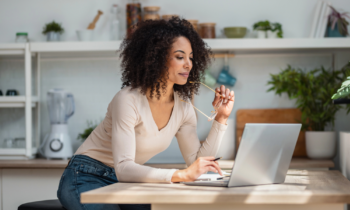 Shot of cheerful attractive woman working with laptop in the kitchen looking for 1099 jobs