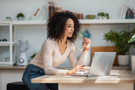 Shot of cheerful attractive woman working with laptop in the kitchen looking for 1099 jobs