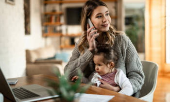 Smiling mother holding small daughter in her lap while talking on the phone at home for blog post best online jobs for stay-at-home moms