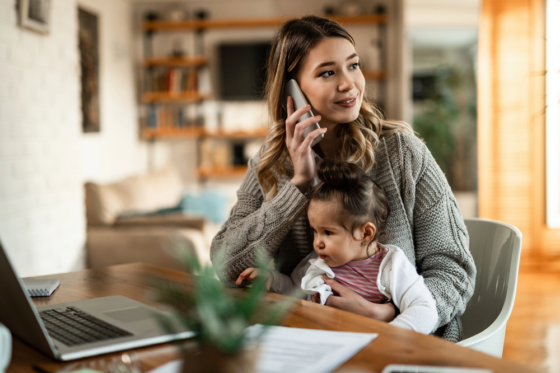 Smiling mother holding small daughter in her lap while talking on the phone at home for blog post best online jobs for stay-at-home moms