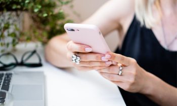Closeup image of a woman using a smartphone while sitting at her home office desk.