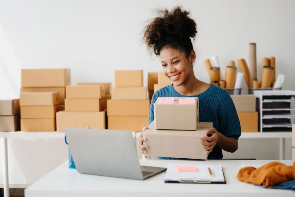 An online reseller using a laptop and packaging items for sale in a home office.