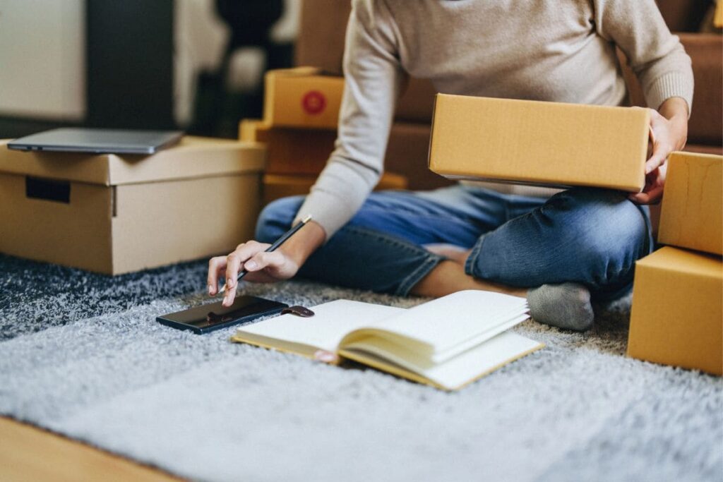 An online reseller sitting on her living room floor, holding boxes and using a calculator.