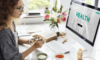 Women eating a bowl of oatmeal with fruit working at her laptop