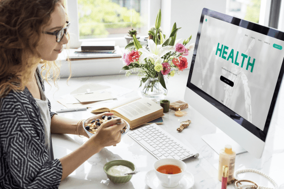 Women eating a bowl of oatmeal with fruit working at her laptop