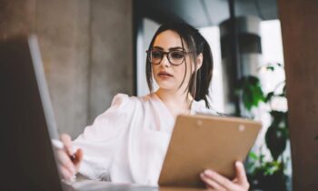 A recruiter sitting at a desk, holding a clipboard, looking at a resume, while using laptop for blog post what to put on a job resume