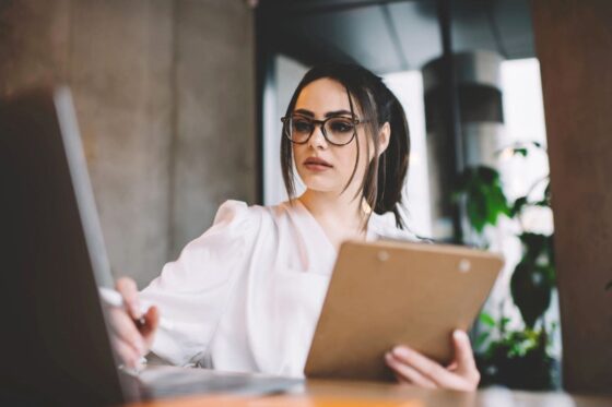 A recruiter sitting at a desk, holding a clipboard, looking at a resume, while using laptop for blog post what to put on a job resume