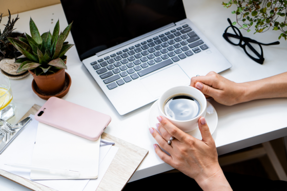 Woman holding cup of coffee studying her work at home courses on her laptop