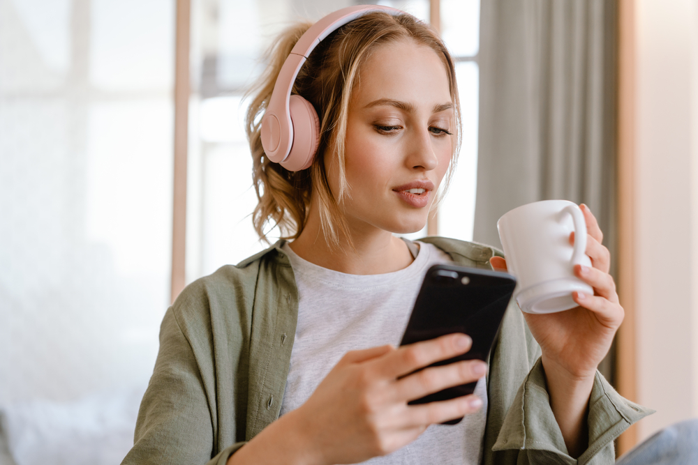 Woman listening to music on phone while drinking coffee