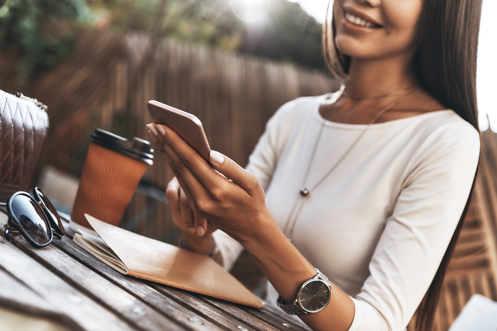 Woman taking paid surveys on smartphone while drinking coffee