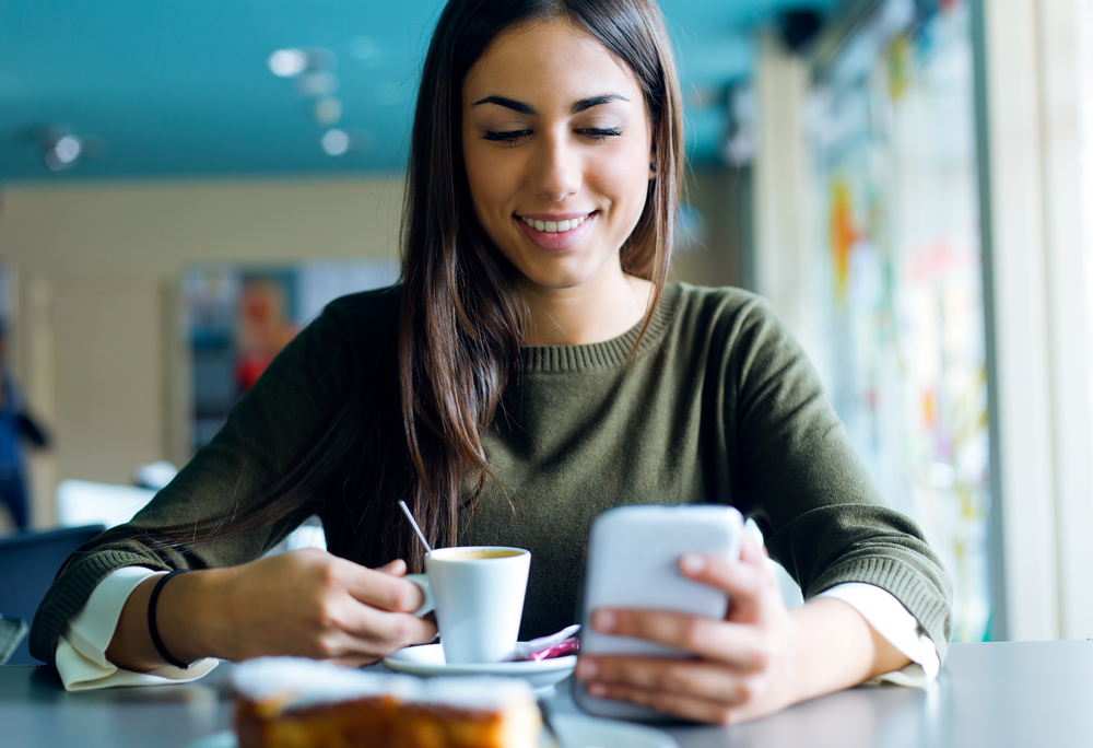 Woman with long hair drinking coffee in a cafe working her mobile phone job