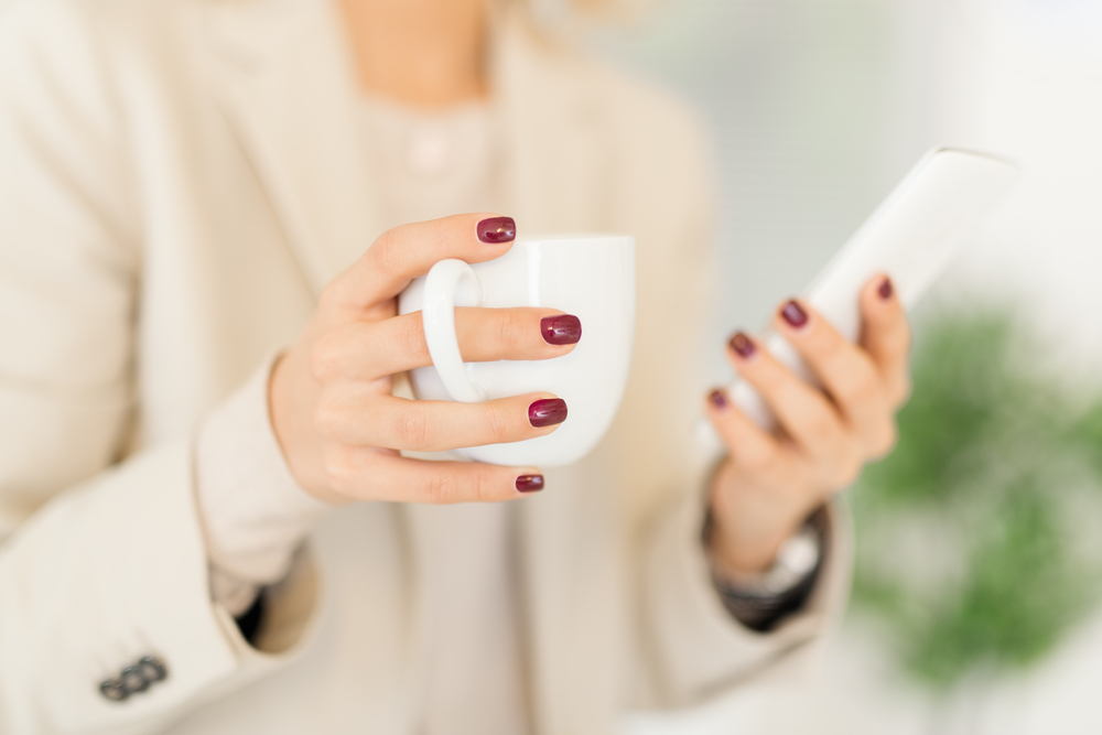 woman with painted finger nails drinking coffee using smartphone apps to make money