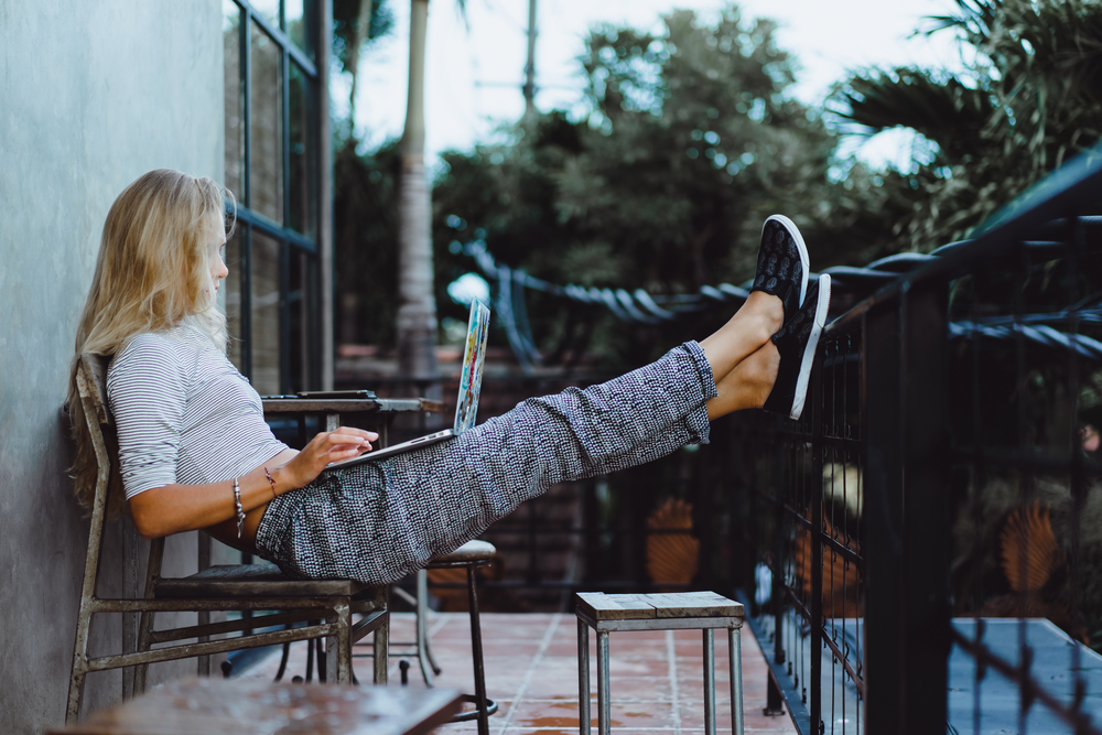 Woman working on her laptop on a balcony with her feet propped up