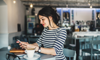 A woman sitting in a coffee shop looking at her mobile phone looking for jobs that pay daily