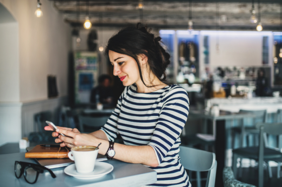 A woman sitting in a coffee shop looking at her mobile phone looking for jobs that pay daily