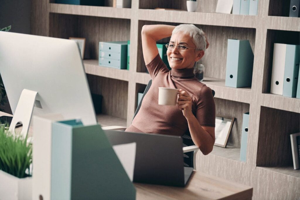 A woman working at her home office desk, with a bookshelf and file storage in the background.