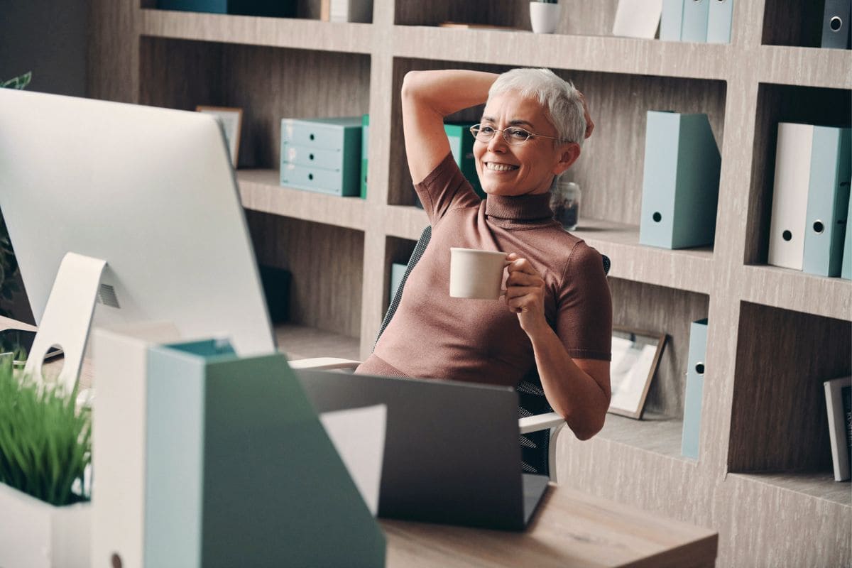 A woman working at her home office desk, with a bookshelf and file storage in the background.
