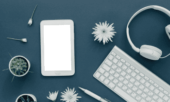 Dark background with light colored laptop, headphone, pen, flowers, and cactus