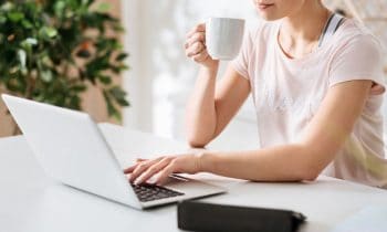 A woman sipping coffee and working from home on a laptop.