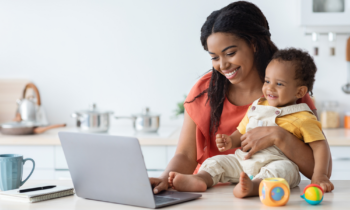 Young mom holding baby working on short tasks on her laptop