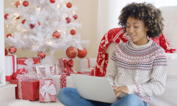 Young woman in a sweater working on laptop in front of Christmas tree
