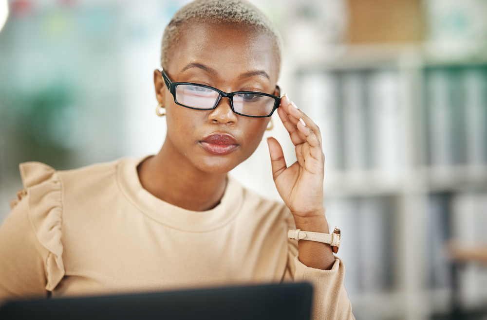 young woman wearing glasses working on a laptop proofreading documents from home