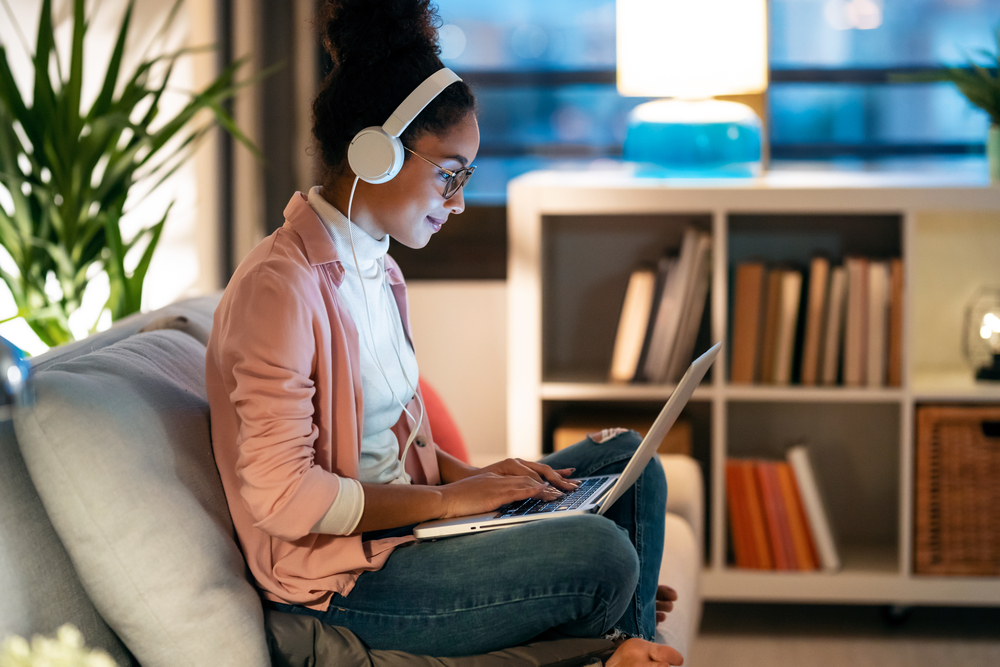 Young woman wearing headphones working her remote night shift job on the sofa