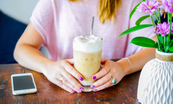Young woman with painted finger nails drinking an iced coffee in a coffee shop