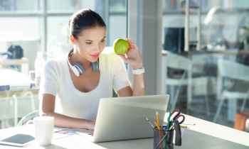 Young woman working on an Apple laptop eating an Apple working from home