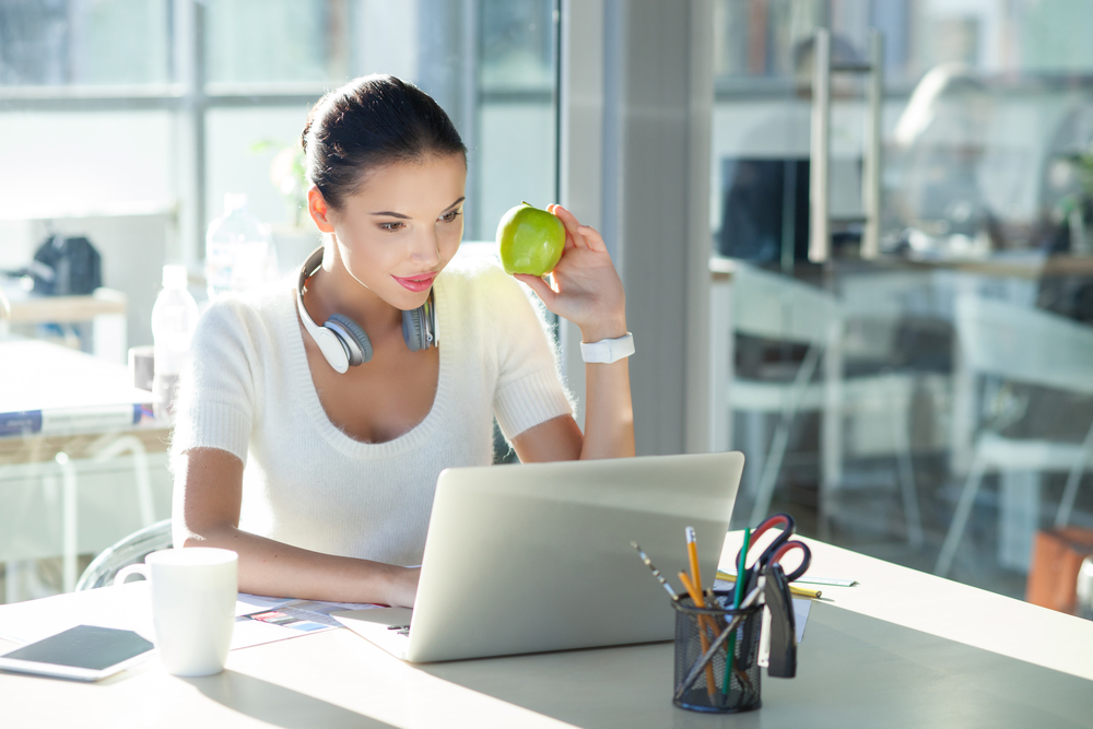 Young woman working on an Apple laptop eating an Apple working from home