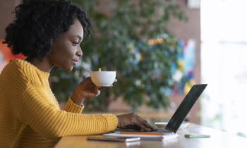 young woman in a sweater drinking coffe working on laptop