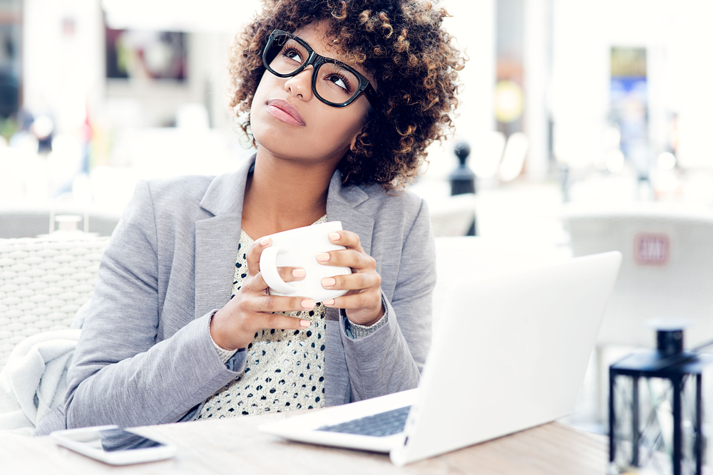 Young woman wearing glasses and drinking coffee wondering where to find legit work from home jobs with no startup fees